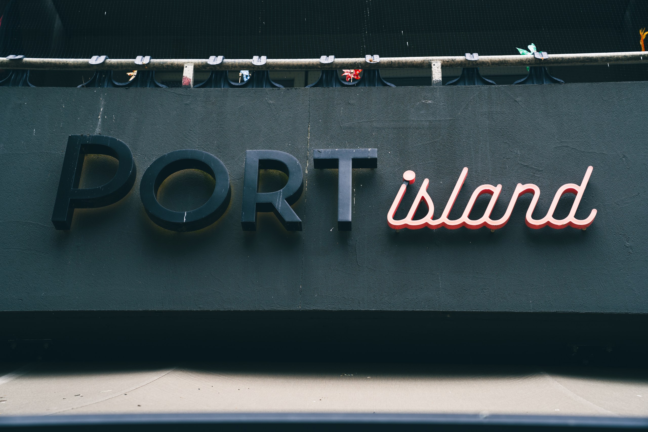 Port Island Hamburg-Schild mit fetten schwarzen "PORT" und rosa Neon "Insel" gegen dunkle Wand. Port Island Hamburg