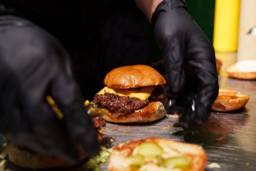 Der Koch mit den schwarzen Handschuhen stellt einen saftigen Rindfleisch-Burger im Hamburger Restaurant Port Island zusammen. Port Island Hamburg