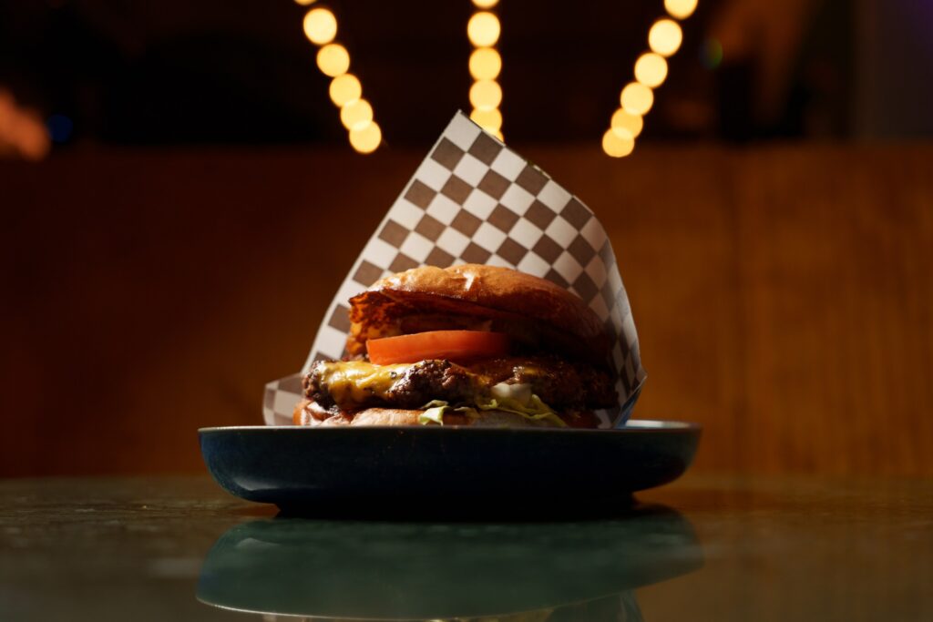 Saftiger Burger mit Salat, Tomate und getoastetem Brötchen auf dunklem Teller im Restaurant Port Island Hamburg. Port Island Hamburg