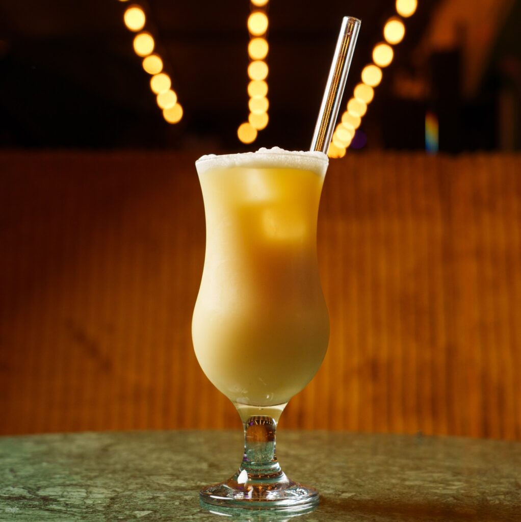 Schaumiger gelber Cocktail im geschwungenen Glas drinks auf der Hafeninsel Hamburg, dahinter leuchtende Lichter. Port Island Hamburg